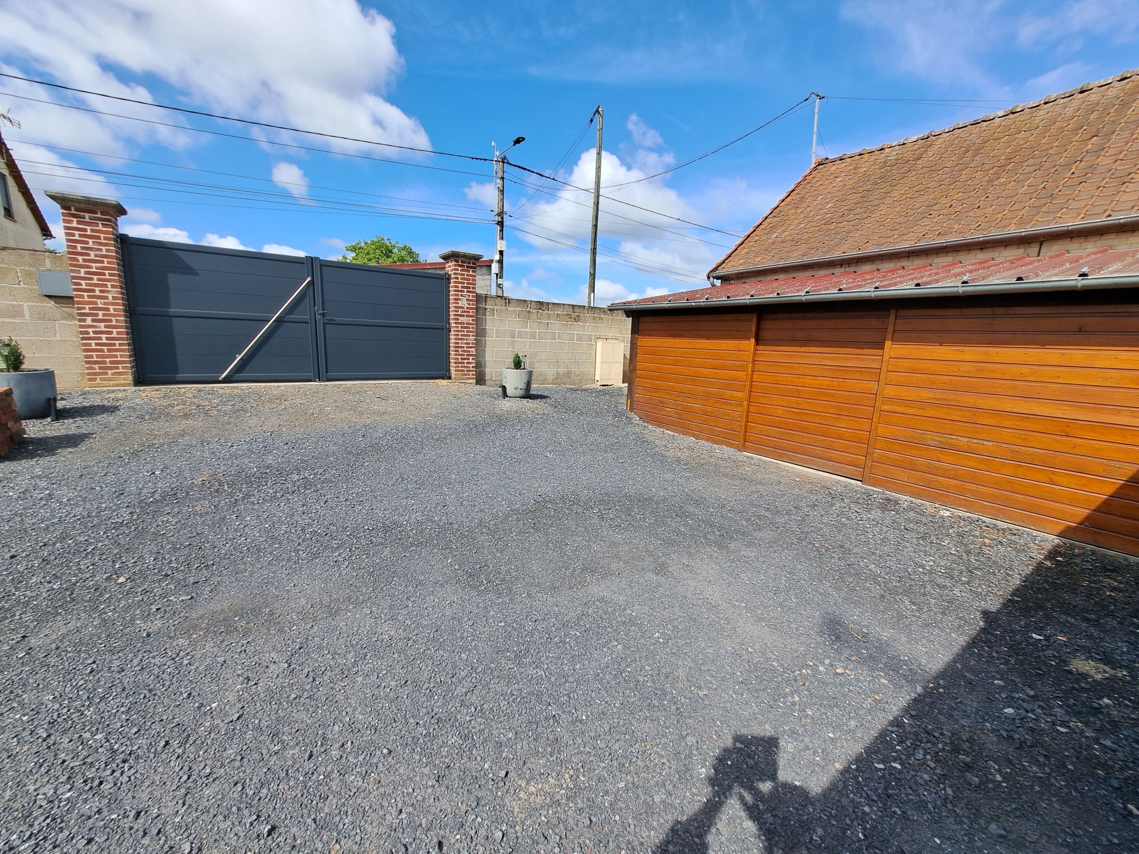 A residential garage with a gravel driveway, a brick wall, and a tiled roof.