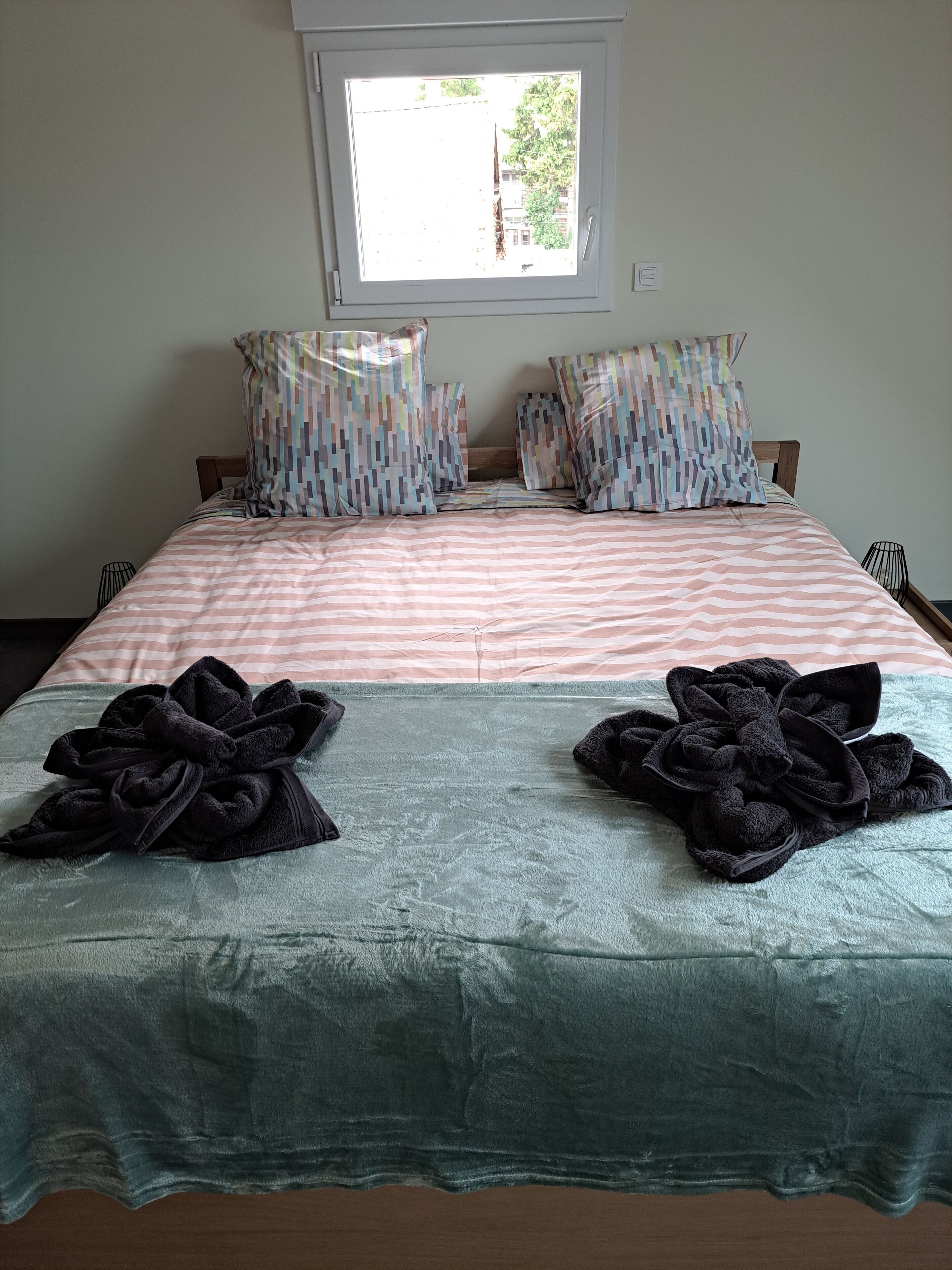 Uma cama com roupa de cama listrada, dois travesseiros com padrão multicolorido e duas toalhas pretas sobre a cama.