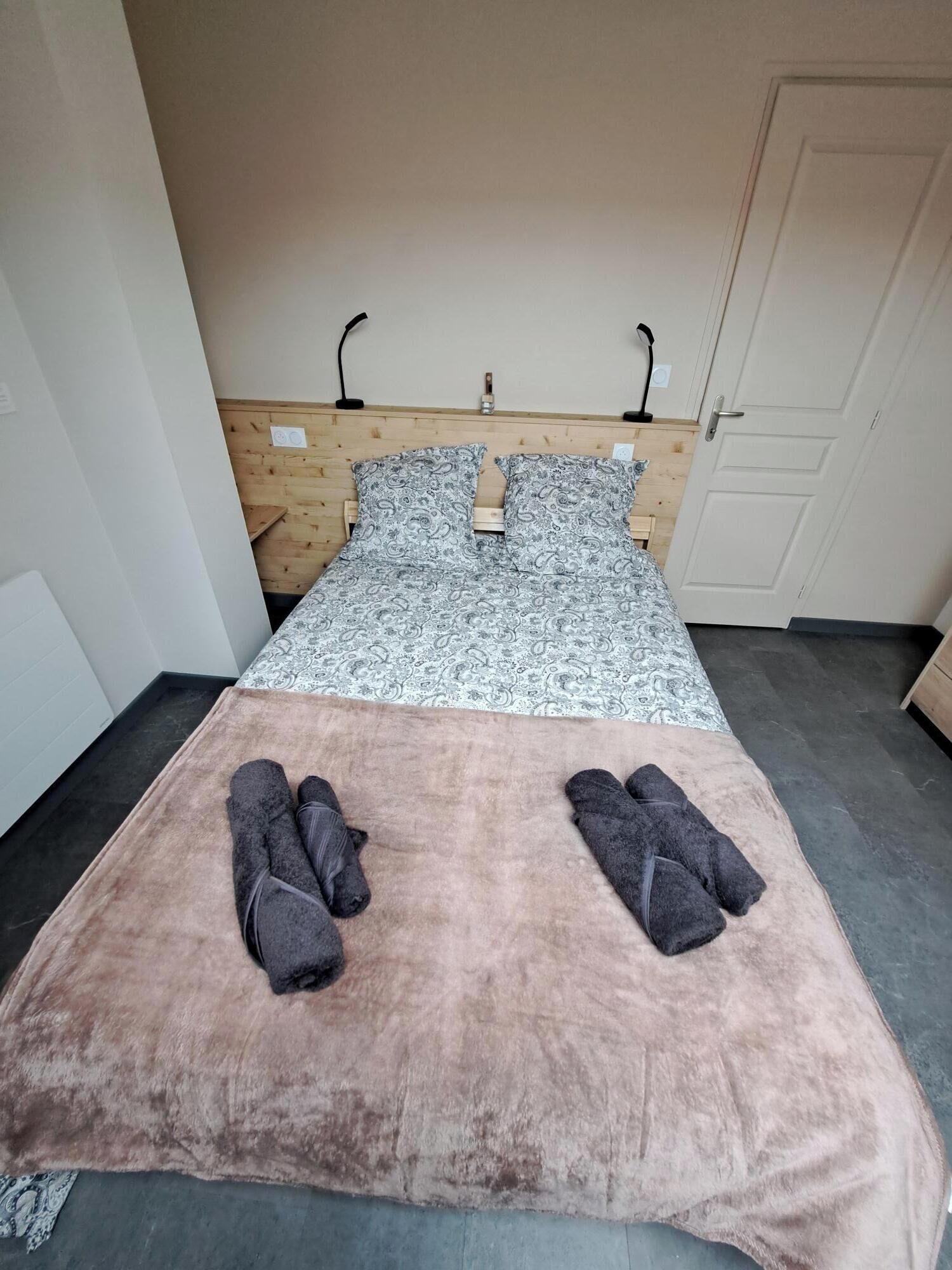 Un lit simple avec une couvre-lit à motifs, deux oreillers et une couverture rose posée sur le sol.