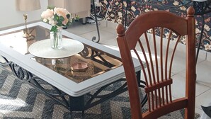 A dining area with a glass-top table, a wooden chair, a patterned rug, and a television on a stand. - Chez Sandrine (La Gacilly)