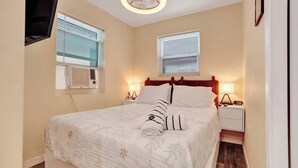 A neatly made bed with a floral bedspread, two bedside tables with lamps, a ceiling fan, and two windows with blinds. - Charming Beachside Studio | Steps to the Beach (Hollywood)