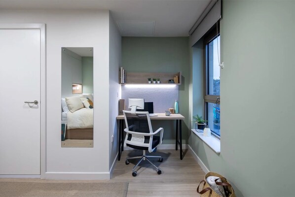 A compact bedroom with a bed, a desk with a computer, and a window.