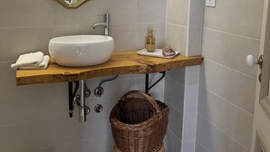 Un baño con lavamanos blanco, un espejo y una estantería de madera.