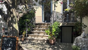 Una escalera de piedra conduce a la entrada de un edificio, rodeada de plantas en macetas y una pizarra anunciando un bar de vinos francés.