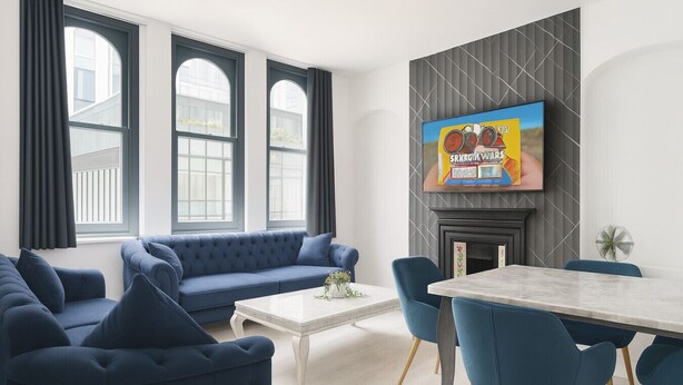 A modern living room with a blue sofa, a coffee table, and a TV mounted on the wall. - Stylish 2-Bedroom Apartment in the Heart of Soho (London)