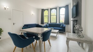 A modern living room with a dining area, featuring a sofa, a table, and a TV mounted on the wall. - Stylish 2-Bedroom Apartment in the Heart of Soho (London)