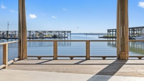 Een houten terras met een metalen hekwerk met uitzicht op een jachthaven met boten en steigers.