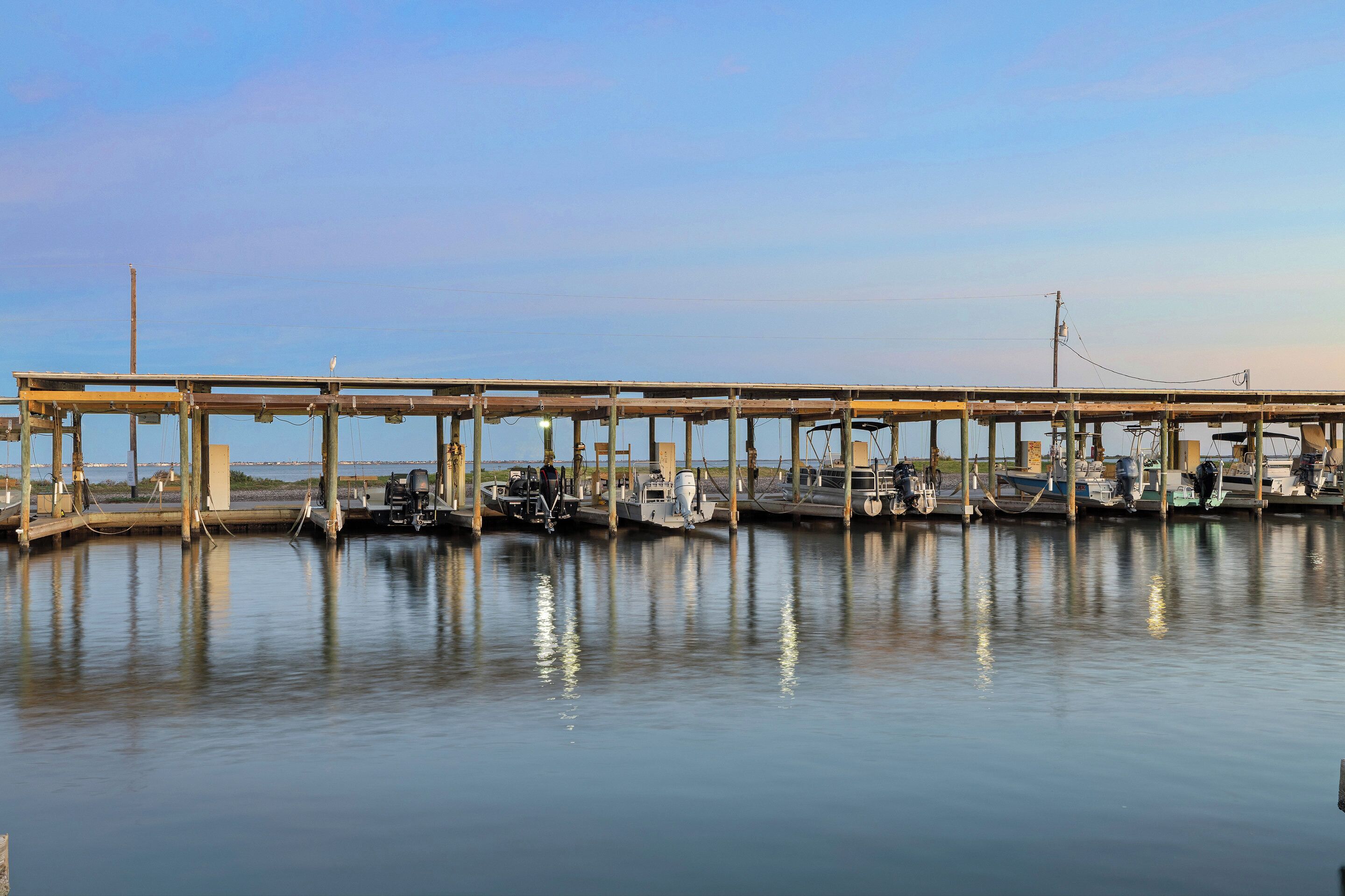 A pier with boats docked, a clear sky, and calm water.