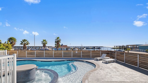 A pool area with a hot tub, lounge chairs, and a view of the beach and pier.