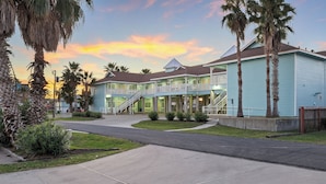 A two-story building with a light blue exterior, a covered walkway, and palm trees.
