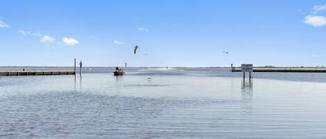 A calm waterfront with a pier extending into the water, a sign indicating a slow area, and a distant structure on the horizon.