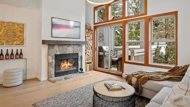 A living room with a fireplace, large windows, a sofa, and a coffee table. - Updated Ski In 3-bedroom townhome in Whistler (Whistler)