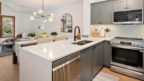 A modern kitchen with a central island, stainless steel appliances, and a dining area with a sofa and table. - Updated Ski In 3-bedroom townhome in Whistler (Whistler)