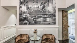 A lobby with a large black and white photograph of a cityscape, two leather armchairs, a small round table, and a decorative vase. - Rhea Silvia Luxury Rooms Spagna (Rome)
