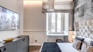 A modern bedroom with a large bed, a grey cabinet, a television, and a window with a view of buildings. - Rhea Silvia Luxury Rooms Spagna (Rome)