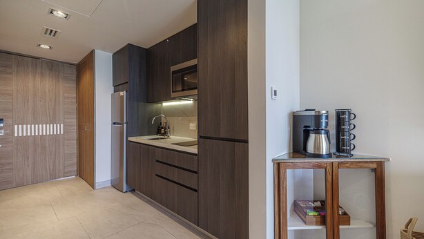 A modern kitchen with dark wood cabinets, a stainless steel refrigerator, and a coffee machine on a wooden table.