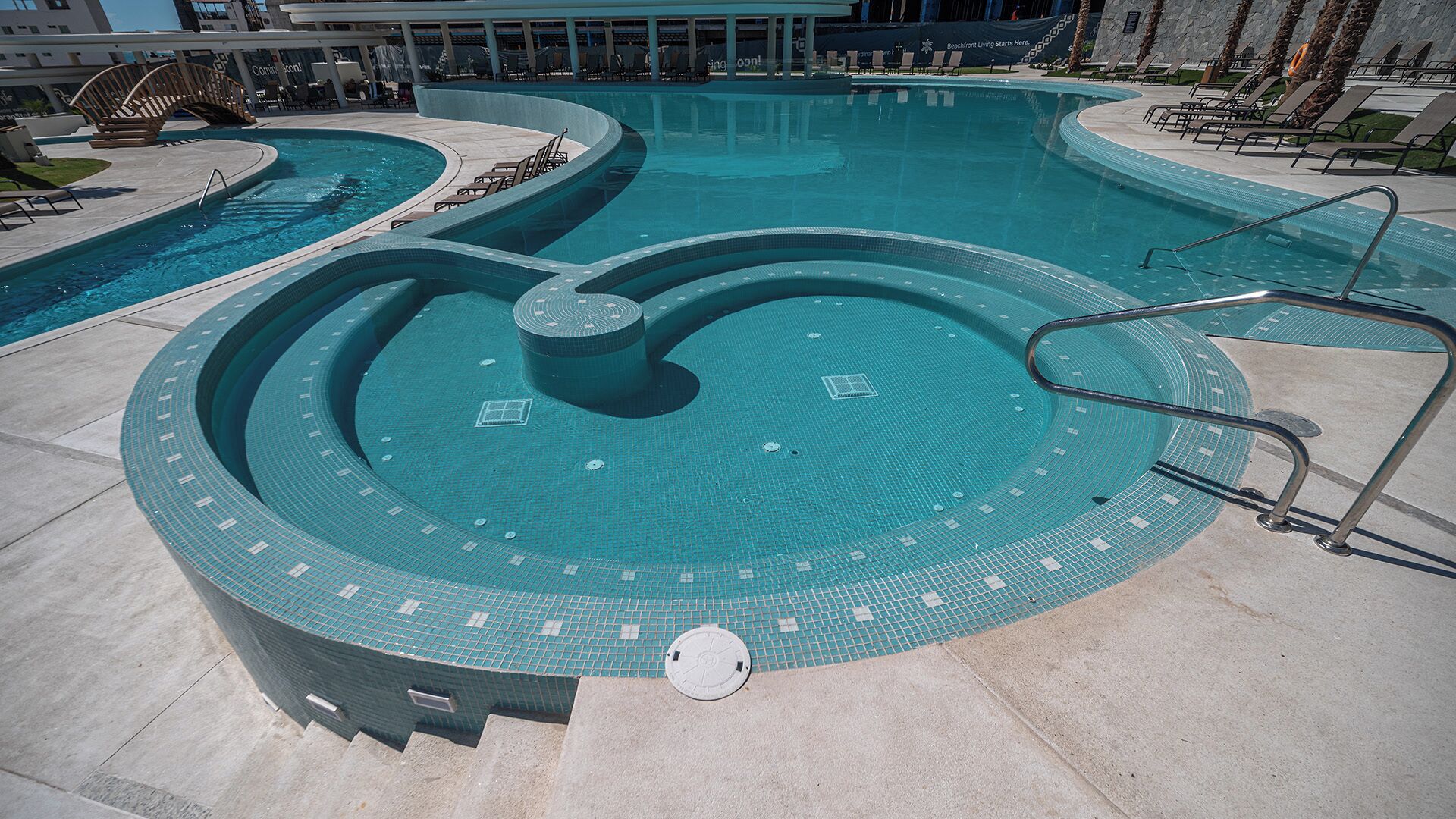 A swimming pool with a circular hot tub in the center, surrounded by lounge chairs and a covered area.