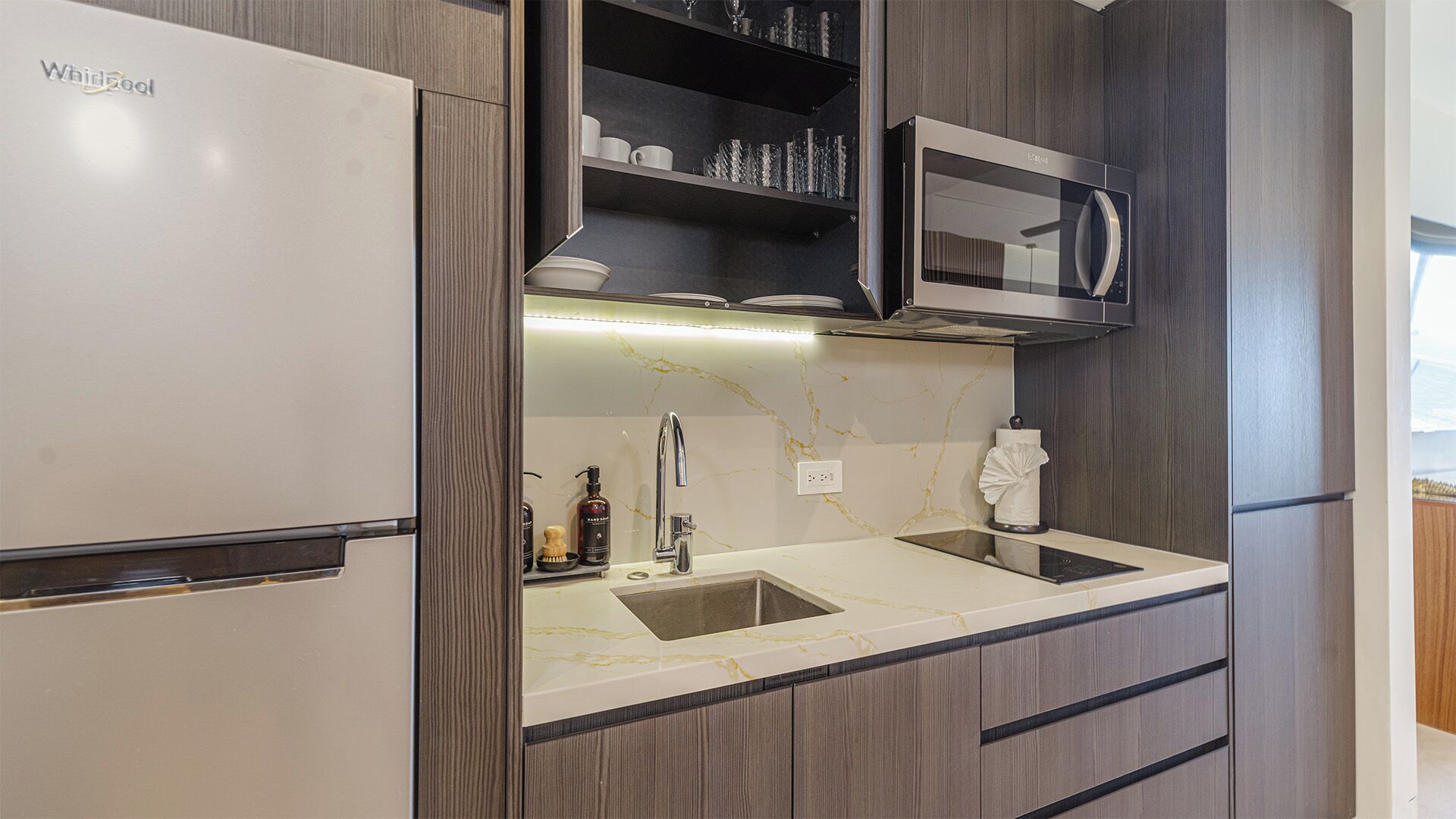 A modern kitchen with a built-in refrigerator, a microwave, and a sink with a marble countertop.