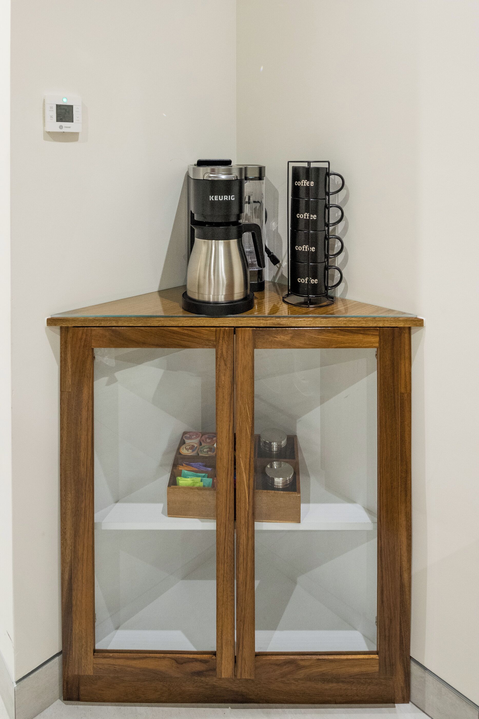A wooden cabinet with a glass door, containing a coffee maker and a mug rack.