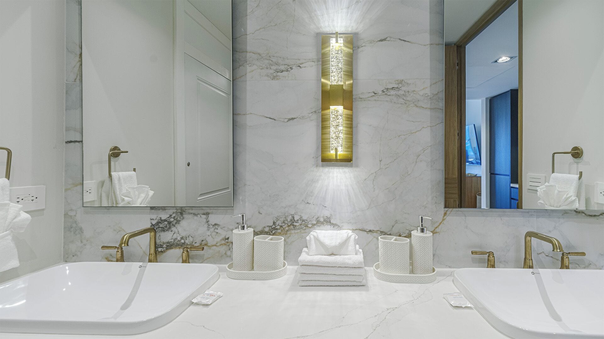 A modern bathroom with two sinks, marble walls, and a vertical light fixture.
