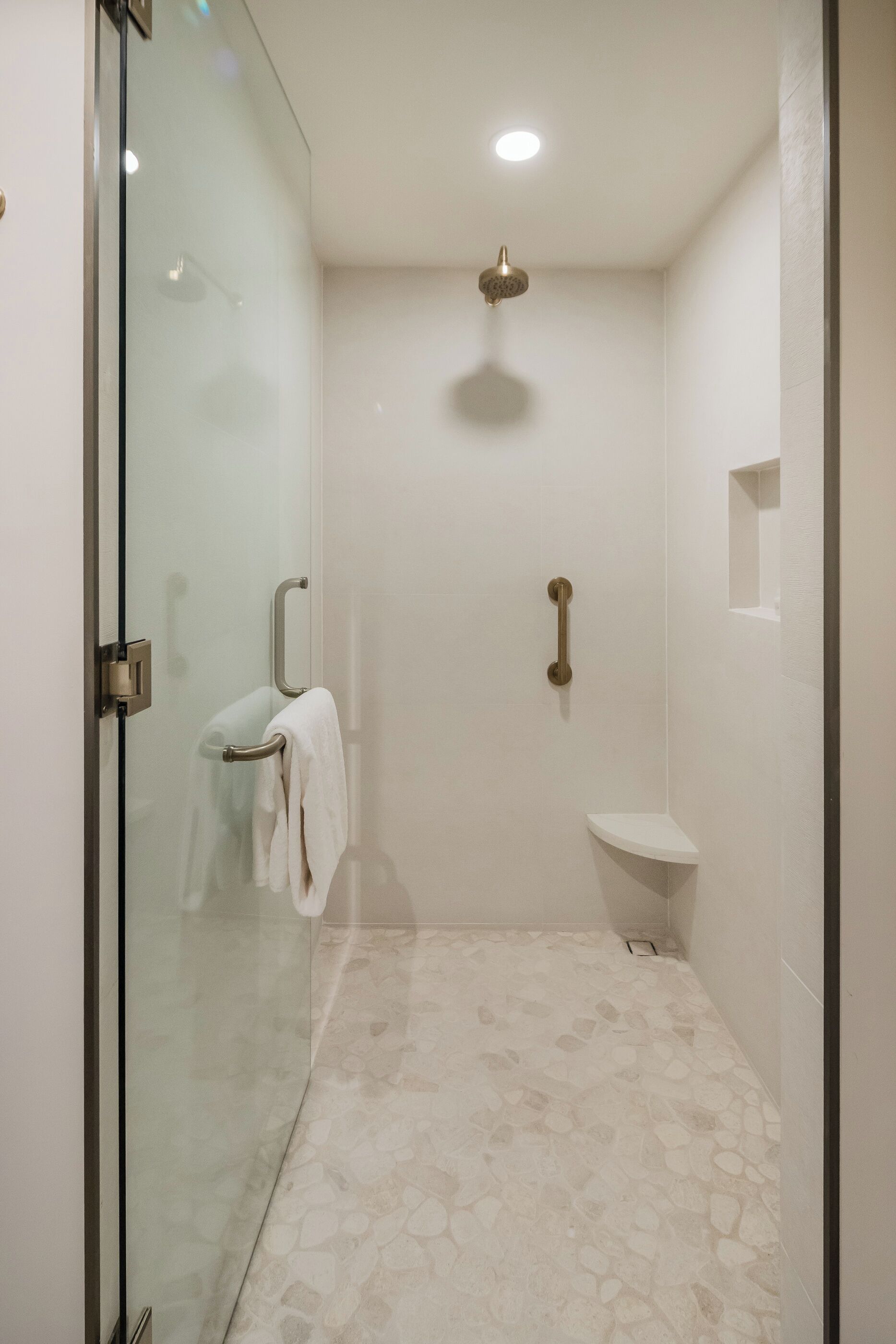 A modern bathroom with a glass shower enclosure, a white tiled floor, and a small white sink.