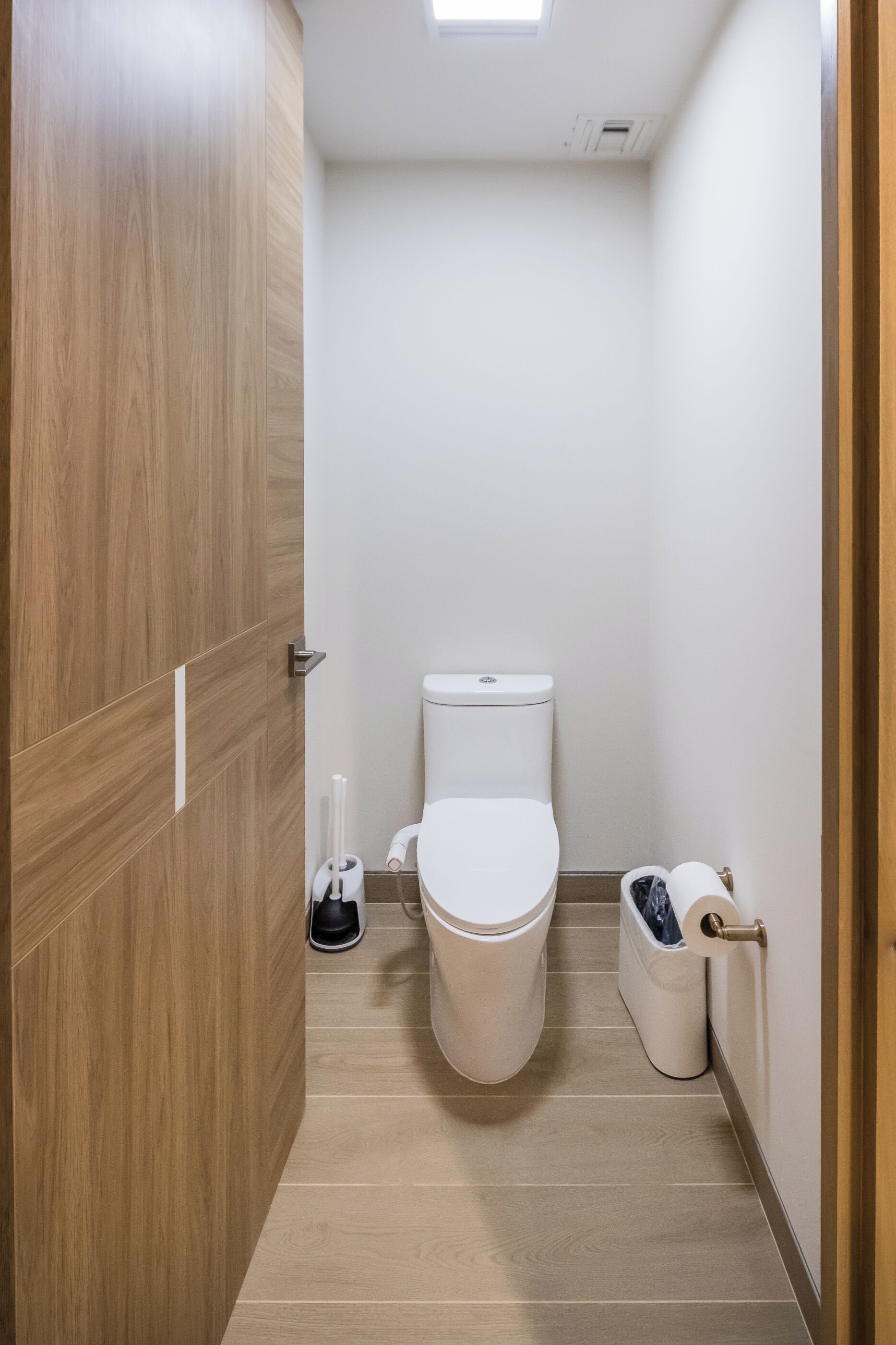 Un baño estrecho con inodoro, un cubo de basura y un dispensador de papel higiénico.