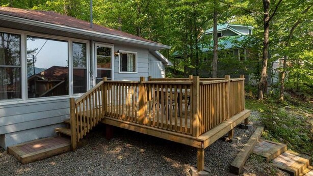 Une maison avec une terrasse en bois, un porche à l’avant et une allée gravillonnée.