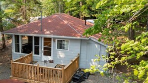 Une petite cabane en bois dotée d’une terrasse, d’un porche couvert et d’un toit rouge, entourée d’arbres.