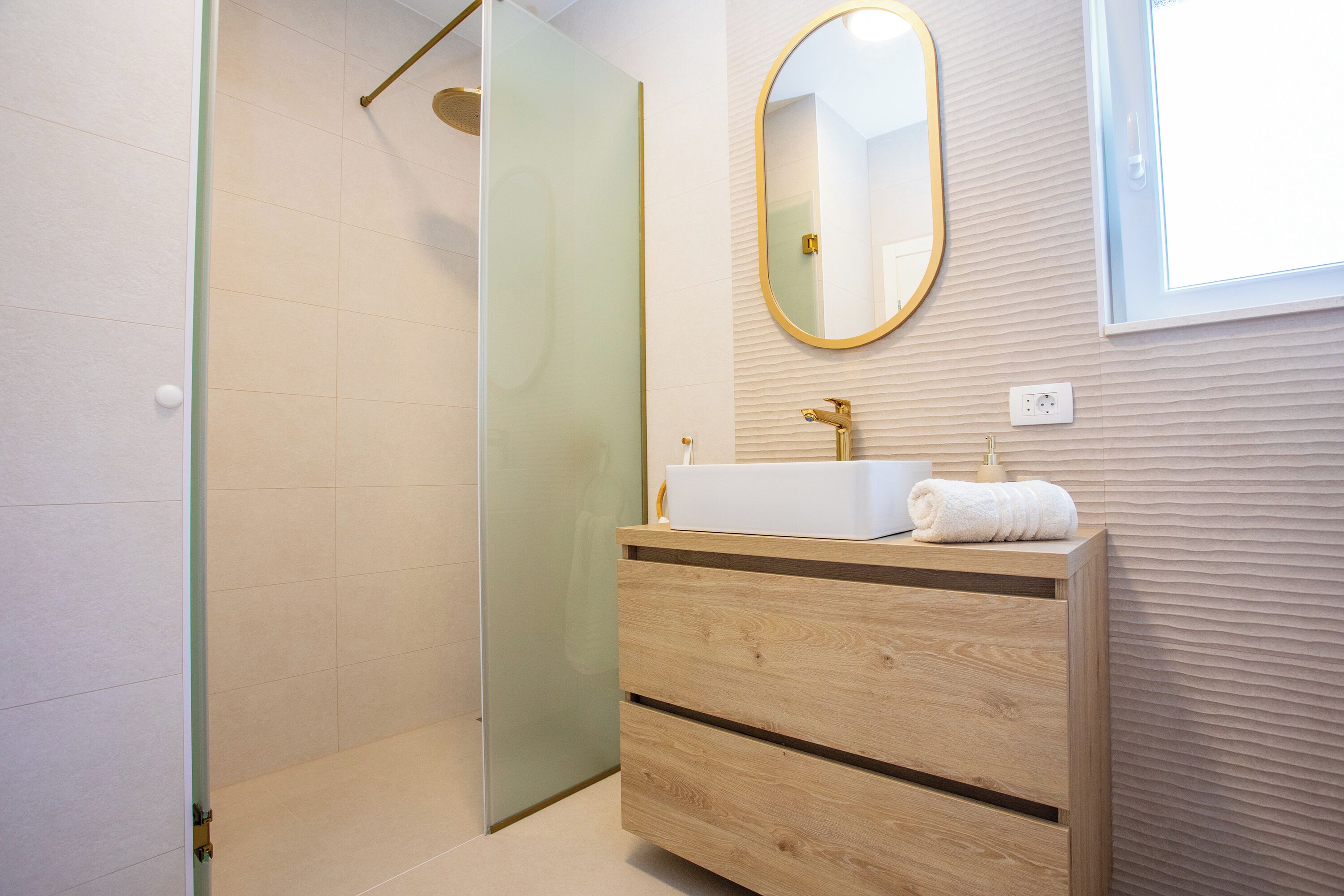 Une salle de bain moderne avec une douche à l’italienne en verre, un meuble-lavabo en bois avec un vasque blanche et un grand miroir mural.