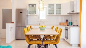 Une cuisine moderne avec des meubles blancs, un réfrigérateur en acier inoxydable, une table à manger avec des chaises jaunes et un luminaire suspendu.