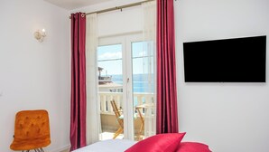 Une chambre d’hôtel avec un lit, une télévision, une chaise et un balcon donnant sur la mer.
