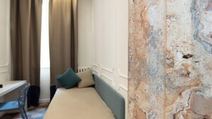 A small, single-bed room with a desk and chair, a window with curtains, and a wall with visible damage. - Nox (Rome)