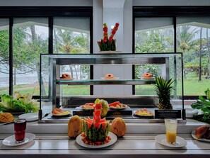 A breakfast buffet with various fruits and pastries, a glass of juice, and a sign about allergens. - Milele Beach Hotel (Mombasa)