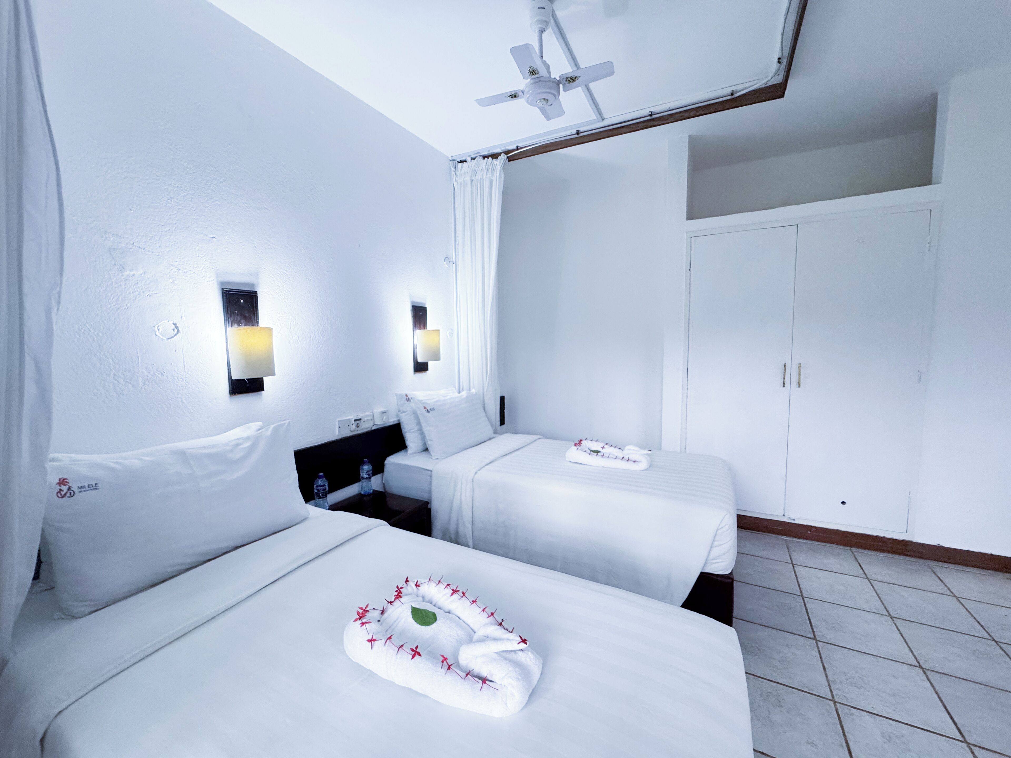 Habitación de hotel con dos camas, un armario y un ventilador de techo.