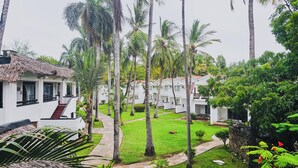 Ein Resort mit weißen Gebäuden, einem Gebäude mit Strohdach und einem gepflegten Garten mit Palmen.