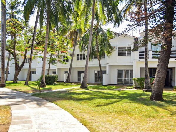 A modern building with a white facade, surrounded by palm trees and a well-maintained lawn.