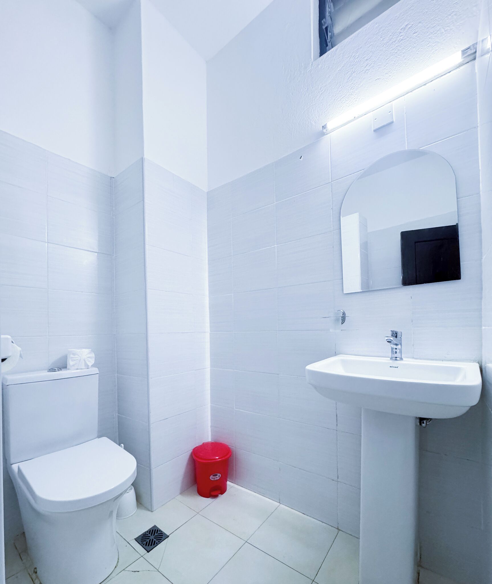 Ein kleines, weißes Badezimmer mit Toilette, Waschbecken und Spiegel.