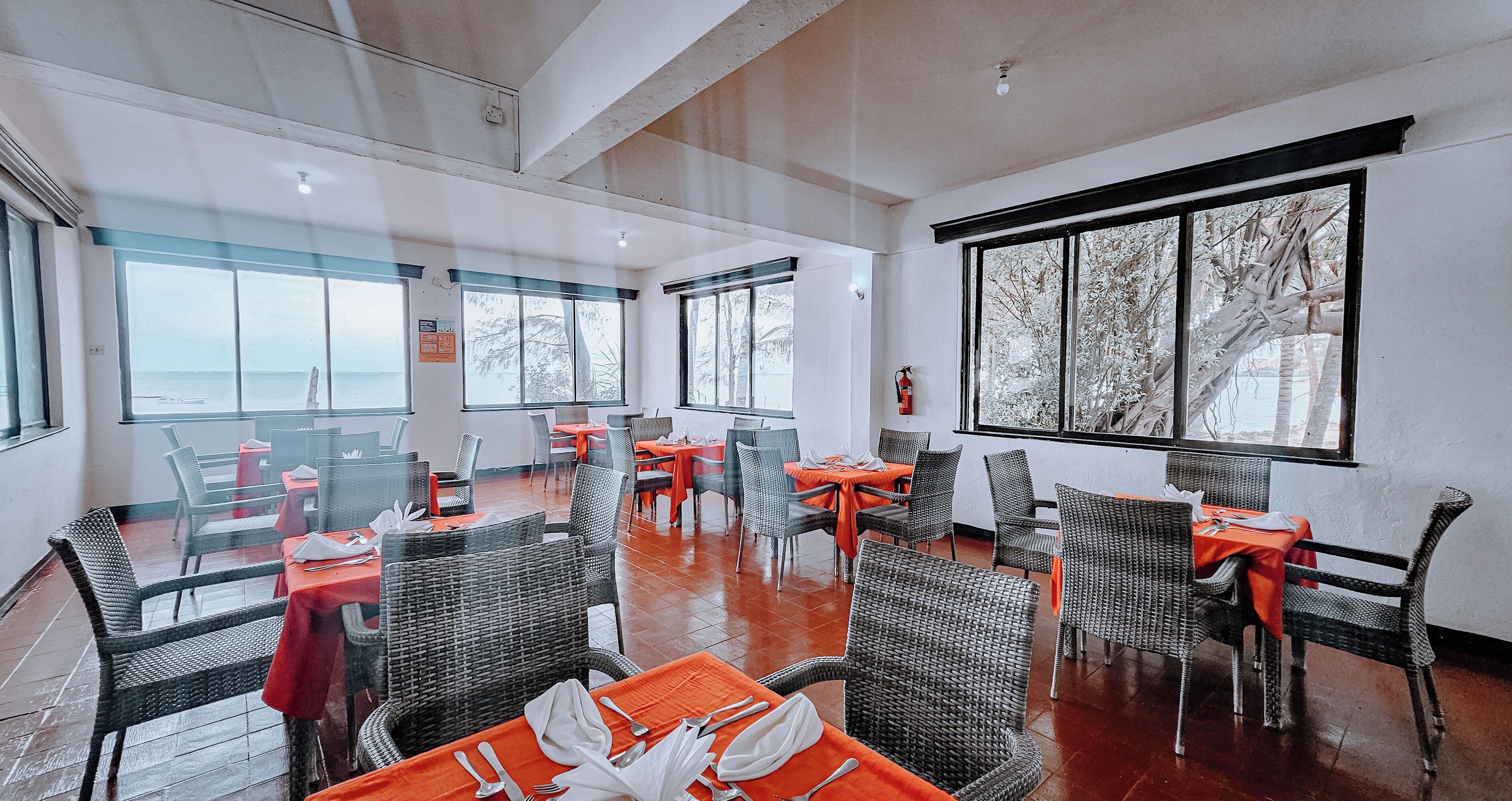 A restaurant with tables and chairs, large windows, and a view of the sea.