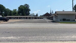 Un motel con aparcamiento, una iglesia al fondo y un camión estacionado a la izquierda.