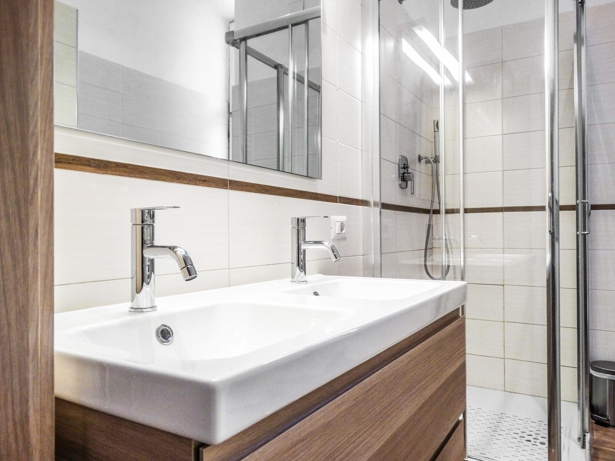 A modern bathroom with a double sink, a mirror, and a glass shower enclosure.
