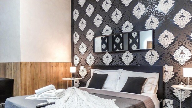 A hotel room with a bed, bedside tables, a mirror, and a patterned wallpaper. - Magic Guest House (Rome)
