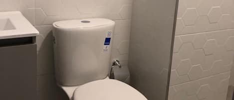 Et badeværelse med toilet, et håndklædestativ med foldede håndklæder og en toiletpapirholder.