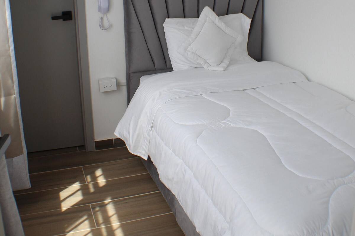 A hotel room with a bed, a bedside phone, and a door.