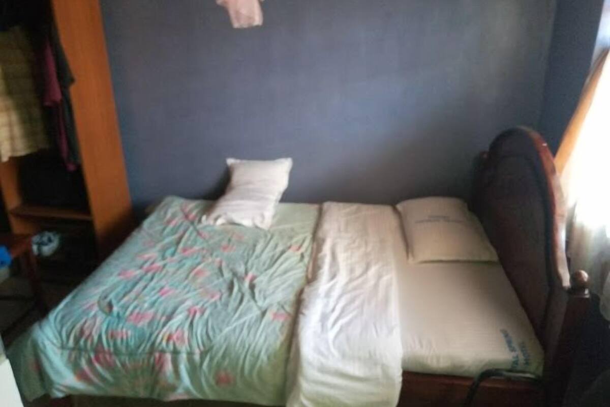 A single bed with a floral bedspread, a white pillow, and a wooden headboard.