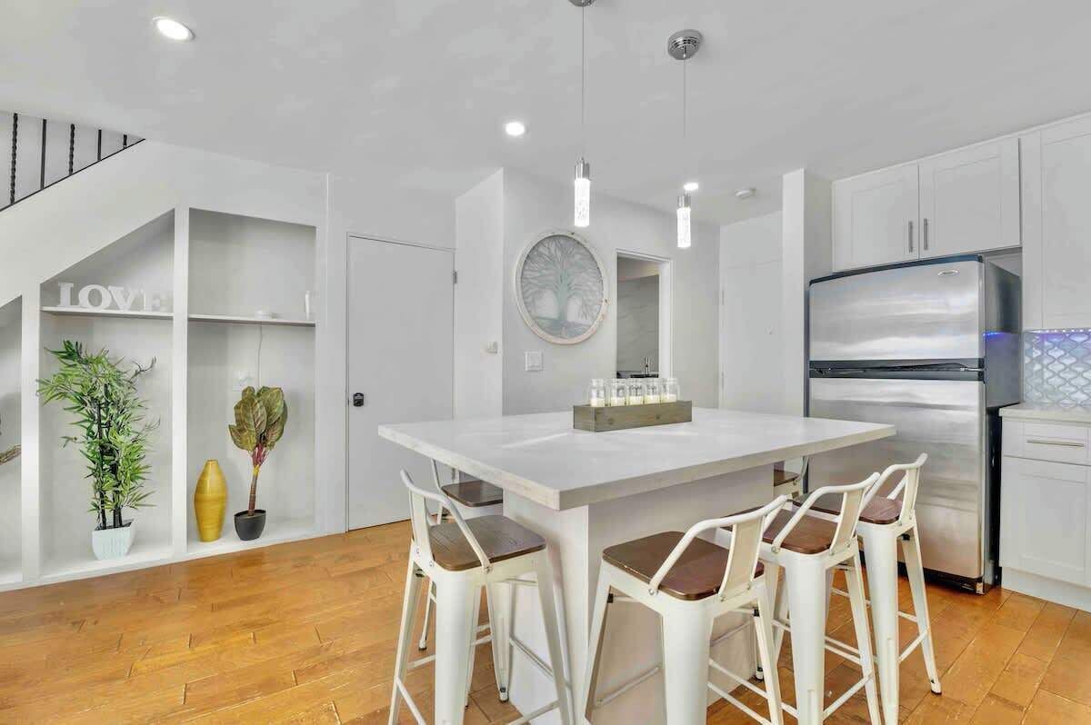Una cocina moderna con una isla central, armarios blancos y un refrigerador de acero inoxidable.