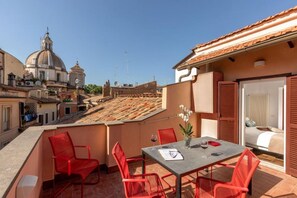 Une terrasse sur le toit avec une table et des chaises, une vue sur des bâtiments historiques et un espace nuit avec un lit.