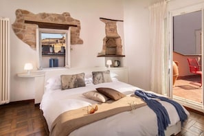 A bedroom with a stone fireplace, a bed with multiple pillows, a nightstand with a lamp, and a view of the outside balcony.