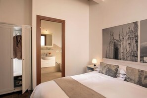 A hotel room with a bed, a nightstand, a mirror, a wardrobe, and a bathroom visible through an open door.