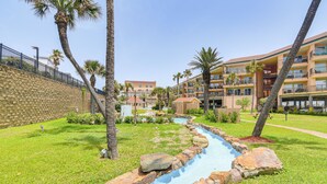 A hotel courtyard with a water feature, palm trees, and a stone wall. - 3 Pools and 2 Hot Tubs, Walk to the Beach (Galveston)