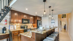 A kitchen with wooden cabinets, a granite countertop, stainless steel appliances, and a bar area with stools. - 3 Pools and 2 Hot Tubs, Walk to the Beach (Galveston)